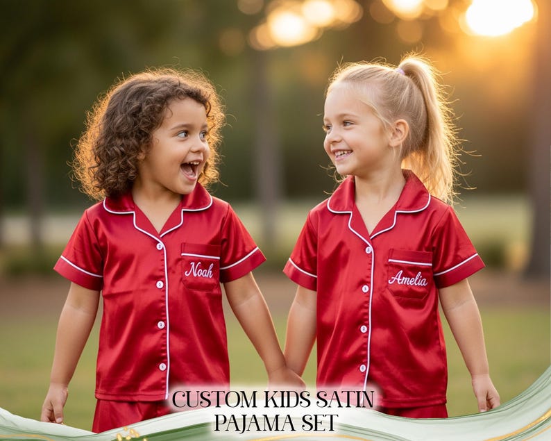 Puede incluir: Dos ni&ntilde;os peque&ntilde;os con conjuntos de pijama de sat&eacute;n rojo a juego con ribetes blancos y nombres personalizados bordados en los bolsillos. El texto "CUSTOM KIDS SATIN PAJAMA SET" se muestra en la parte inferior de la imagen.
