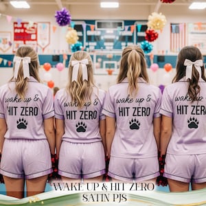 Peut inclure: Quatre ensembles de pyjamas en satin lavande assortis. Chaque ensemble comprend un haut à manches courtes et un short, avec une bordure noire. Les hauts affichent le texte "wake up & HIT ZERO" et une empreinte de patte. Des nœuds blancs ornent les cheveux.