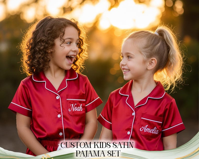 Puede incluir: Dos ni&ntilde;os con conjuntos de pijama de sat&eacute;n rojo con ribetes blancos y bordados personalizados. Un conjunto de pijama est&aacute; bordado con "Noah" y el otro con "Amelia". La imagen incluye el texto "CUSTOM KIDS SATIN PAJAMA SET".