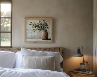 May include: A bedroom scene featuring a framed painting of a vase with olive branches. The painting hangs above a bed with white linens and a textured beige pillow. A small wooden side table holds a lamp and books.