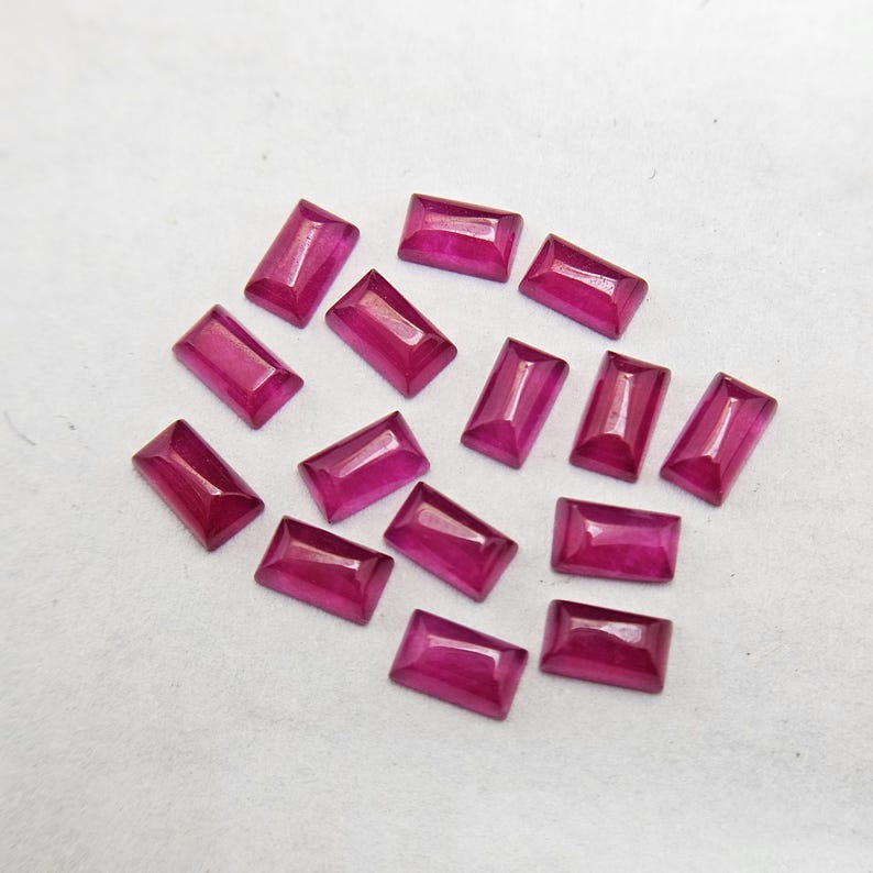 Pode incluir: Uma cole&ccedil;&atilde;o de pedras preciosas retangulares, vermelho escuro. Cada gema tem uma superf&iacute;cie polida e uma apar&ecirc;ncia ligeiramente transl&uacute;cida. As gemas est&atilde;o dispostas sobre uma superf&iacute;cie branca, mostrando sua cor e forma vibrantes.