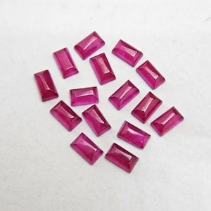 Pode incluir: Uma cole&ccedil;&atilde;o de pedras preciosas retangulares, magenta escuro. As gemas est&atilde;o dispostas sobre uma superf&iacute;cie branca, mostrando suas facetas polidas e sua cor rica. Provavelmente rubis, adequadas para joias.