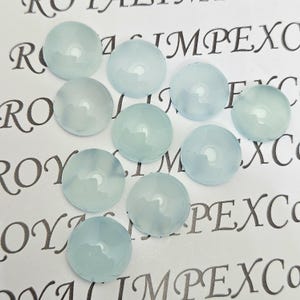 K&ouml;nnte beinhalten: Eine Ansammlung von zehn runden, hellblauen Cabochons. Die Cabochons sind auf einer wei&szlig;en Oberfl&auml;che mit aufgedrucktem Text angeordnet. Die Edelsteine haben ein glattes, poliertes Aussehen und sind leicht durchscheinend.