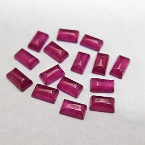 Pode incluir: Uma cole&ccedil;&atilde;o de pedras preciosas de rubi retangulares e polidas. Cada gema tem uma cor magenta profunda e uma superf&iacute;cie lisa e refletora. As gemas est&atilde;o dispostas sobre uma superf&iacute;cie de cor clara, mostrando sua tonalidade e forma vibrantes.