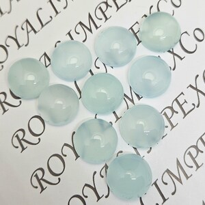 K&ouml;nnte beinhalten: Zehn hellblaue, runde Cabochon-Edelsteine. Die polierten Steine haben eine gl&auml;nzende Oberfl&auml;che und sind auf einer wei&szlig;en Oberfl&auml;che mit aufgedrucktem Text angeordnet. Geeignet f&uuml;r Schmuckherstellung und Bastelarbeiten.
