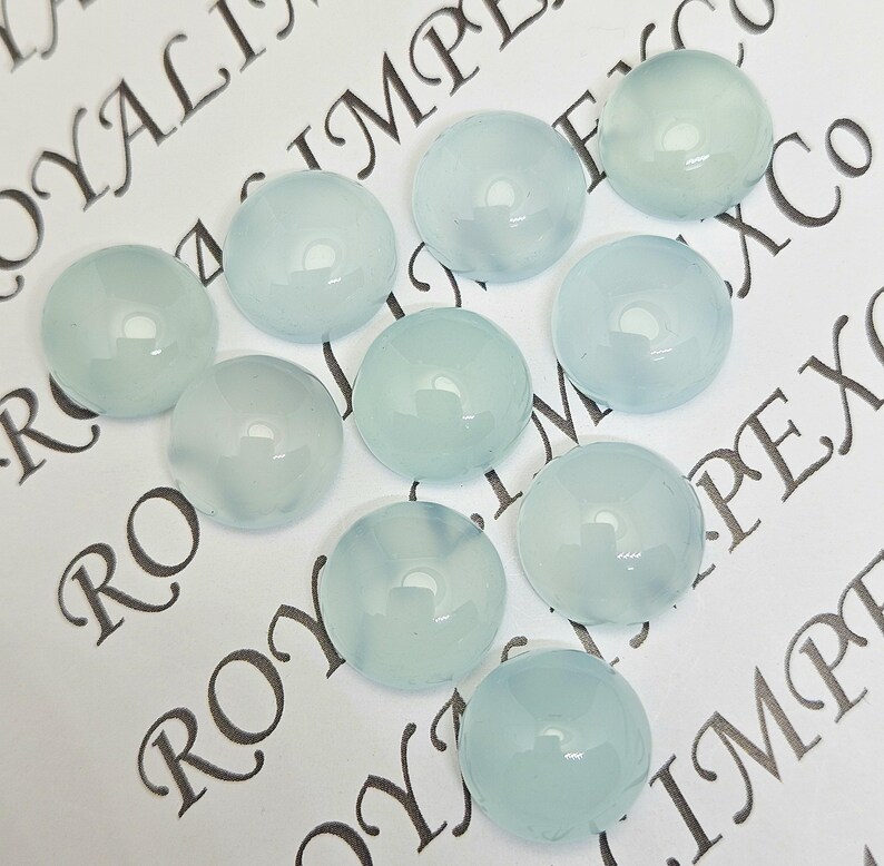 K&ouml;nnte beinhalten: Zehn hellblaue, runde Cabochon-Edelsteine. Die polierten Steine haben eine gl&auml;nzende Oberfl&auml;che und sind auf einer wei&szlig;en Oberfl&auml;che mit aufgedrucktem Text angeordnet. Geeignet f&uuml;r Schmuckherstellung und Bastelarbeiten.