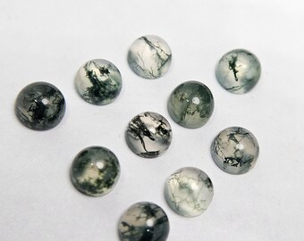 May include: A collection of ten round, polished gemstones. The stones feature a translucent base with intricate, tree-like inclusions in shades of green and black. The cabochons are arranged on a white surface.