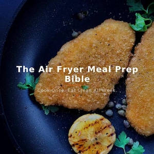 Puede incluir: Una vista superior de una sartén oscura con dos filetes de pollo empanados, una rodaja de limón a la parrilla y ramitas de perejil. El texto "The Air Fryer Meal Prep Bible" se muestra, junto con "Cook Once. Eat Clean All Week."
