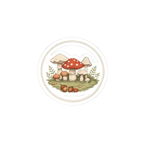 May include: A circular sticker with a watercolour illustration of several mushrooms in different sizes and colours, including red with white spots, beige, and orange. The mushrooms are surrounded by green foliage and acorns, within a white border.