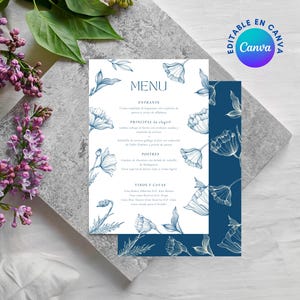 Puede incluir: Un menú de boda con un diseño floral. El menú es blanco con ilustraciones florales azules y texto. El menú está sobre una superficie gris con flores moradas y hojas verdes en el fondo. Las palabras "MENU" y "EDITABLE EN CANVA" son visibles.