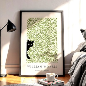 May include: A framed art print with a black cat peeking from behind a green and white leaf pattern. The print includes the text "WILLIAM MORRIS ART AND CATS EXHIBITION". A black lamp, a book, and a coffee cup are in the foreground.