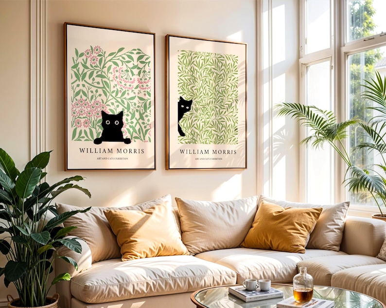 May include: Two framed art prints featuring black cat illustrations. One print has a pink floral background, the other a green leafy design. Both prints have the text "WILLIAM MORRIS" and "ART AND LIFE EXHIBITIONS" in a serif font.