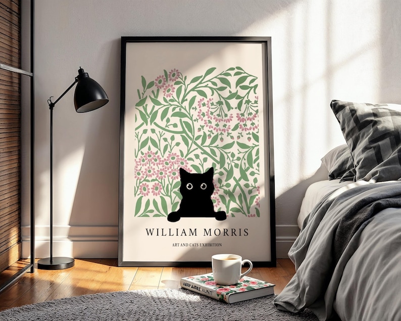 May include: A framed art print featuring a black cat peeking over a floral design in pink and green. The print includes the text "WILLIAM MORRIS ART AND CATS EXHIBITION" in black. A black floor lamp and a cup of coffee are in the foreground.