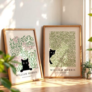 May include: Two framed art prints featuring a black cat peeking out from behind foliage. The prints have a light background with green and pink floral patterns. The text "WILLIAM MORRIS ART AND CATS EXHIBITION" is at the bottom of each print.