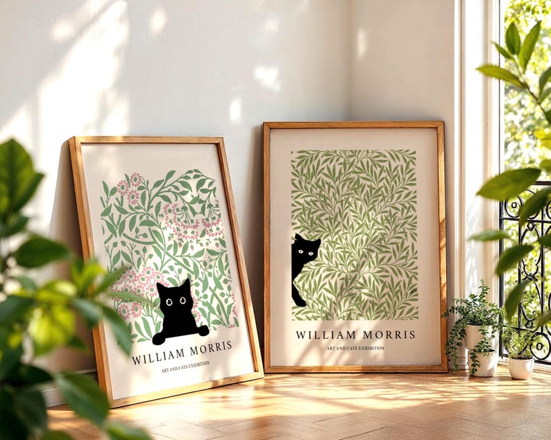 May include: Two framed art prints featuring a black cat peeking out from behind foliage. The prints have a light background with green and pink floral patterns. The text "WILLIAM MORRIS ART AND CATS EXHIBITION" is at the bottom of each print.