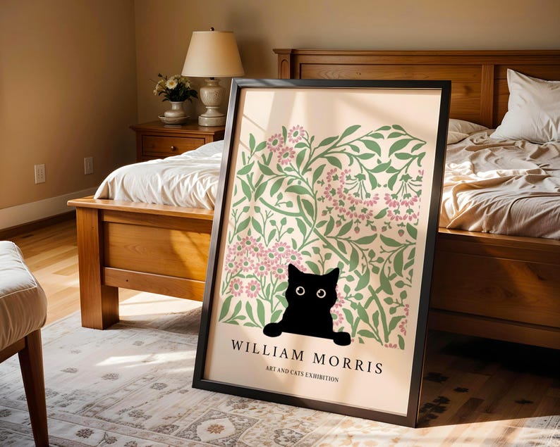 May include: Framed art print featuring a black cat peeking out from behind a floral design in green and pink. The print has the text "WILLIAM MORRIS ART AND CATS EXHIBITION" in black, set against a cream background.