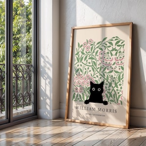 May include: A framed art print featuring a black cat peeking out from a floral design with pink and green accents. The print includes the text "WILLIAM MORRIS ART AND CATS EXHIBITION" in a wooden frame.