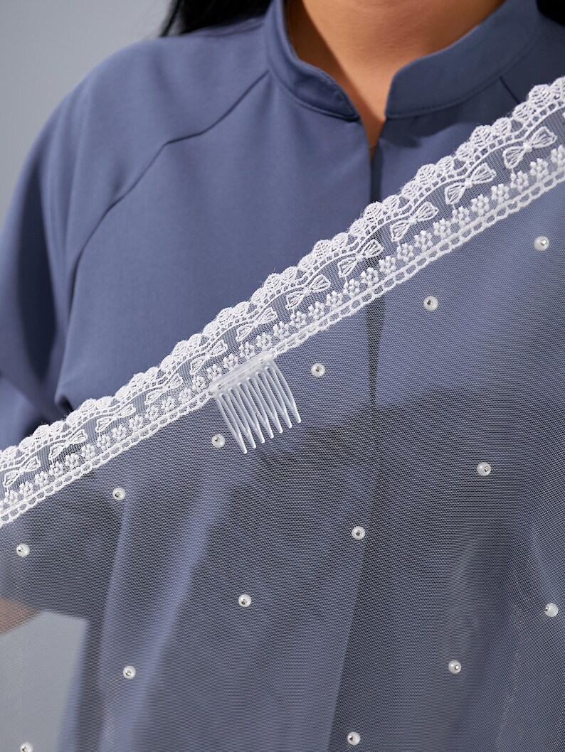 A close-up view of a person wearing a blue shirt with a white lace-trimmed veil draped over their head.