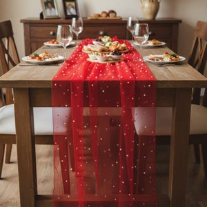 May include: A dining table set for a meal, with a red table runner adorned with white polka dots. The table is set with plates, wine glasses, and a food centerpiece. The wooden table and chairs create a warm, inviting atmosphere.