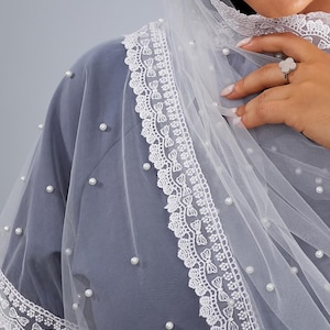 A close-up of a person wearing a gray dress with a white lace-trimmed veil and a ring on their finger.