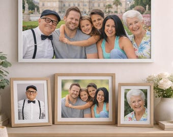 May include: A framed family portrait hangs on a wall above a wooden table. Two smaller framed photos and a vase of white flowers sit on the table. The family photo features a group of smiling people in front of a building.