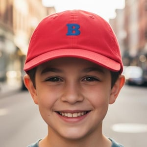 May include: A bright red baseball cap featuring a prominent, embroidered blue letter B centered on the front panel. The cap has a structured crown, a curved brim, and a classic six-panel design, providing a clean and simple look for everyday wear.