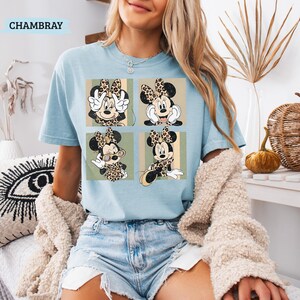 May include: Light blue t-shirt with a graphic of Minnie Mouse in four panels. Each panel features Minnie in a different pose, wearing a leopard print bow and outfit. The word "CHAMBRAY" is printed at the top left of the shirt.