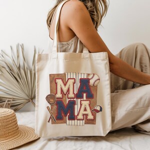 May include: A cream-colored tote bag with the word "MAMA" in a baseball-themed design. The design includes a baseball, glove, bat, and cap. The letters are in red, white, and blue, with a brown background.