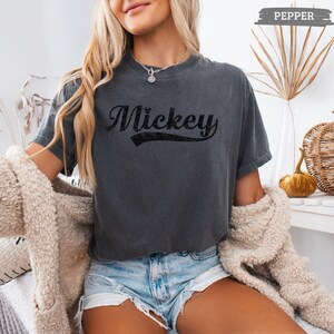 Puede incluir: Camiseta gris oscuro con el nombre "Mickey" en negro, con una tipograf&iacute;a de estilo vintage. La camiseta tiene un estilo informal, con un aspecto ligeramente descolorido. La palabra "Pepper" est&aacute; en una pancarta en la parte superior.