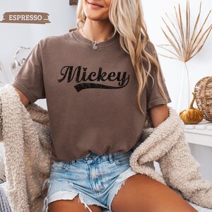 Puede incluir: Camiseta color espresso con el nombre "Mickey" en una escritura negra de estilo vintage. La camiseta de manga corta tiene cuello redondo. La palabra "Espresso" est&aacute; impresa en un peque&ntilde;o cuadro en la esquina superior izquierda.