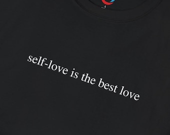 May include: Black t-shirt with the white text "self-love is the best love". The crew neck t-shirt has a small logo in the upper right corner. The t-shirt is folded.