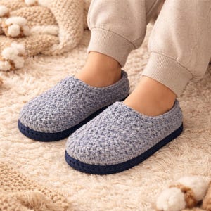Peut inclure: Une paire de pantoufles en crochet bleu clair avec une semelle bleu foncé. Les pantoufles sont faites d'un fil texturé et sont conçues pour être portées à l'intérieur. Elles sont posées sur un tapis crème.