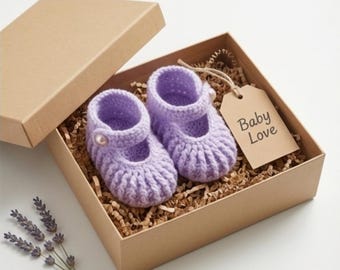 May include: A pair of lavender crochet baby shoes with a pearl button, presented in a brown gift box with shredded paper. A tag with the words "Baby Love" hangs from the box. A sprig of lavender is placed near the box.