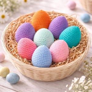 May include: A wicker basket filled with colorful, crocheted Easter eggs. The eggs are in shades of orange, purple, teal, pink, light blue, and mint green, nestled on a bed of straw. A few pastel eggs are scattered around the basket.