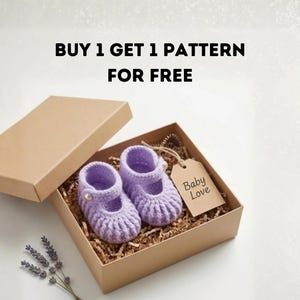 Pode incluir: Um par de sapatos de bebê de crochê lilás com botões, apresentados em uma caixa de presente marrom com papel picado. Uma etiqueta diz "Baby Love". O texto "BUY 1 GET 1 PATTERN FOR FREE" está no topo.