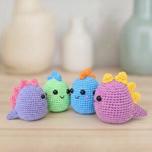 Puede incluir: Cuatro juguetes de dinosaurios de ganchillo de colores. Cada dinosaurio es de un color diferente: morado con espinas rosas, verde con espinas azules, azul con espinas naranjas y morado con espinas amarillas. Tienen ojos negros y caras sonrientes.