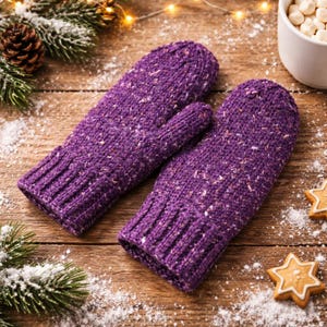 May include: A pair of knitted purple mittens with flecks of white and other colours. The mittens are on a wooden surface with pine needles, a pine cone, and a cup of marshmallows in the background. The mittens have a ribbed cuff.