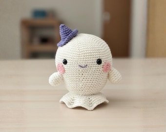 May include: A handmade, crocheted ghost doll with a smiling face, rosy cheeks, and a small purple witch hat. The ghost has small arms and a ruffled base, perfect for Halloween or spooky decor.