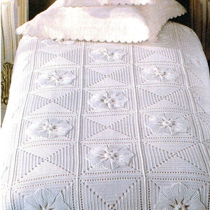 Könnte beinhalten: Weiß gehäkelte Tagesdecke mit floralem Design. Die Tagesdecke besteht aus Quadraten mit einer erhabenen Blume in der Mitte jedes Quadrats. Die Tagesdecke liegt auf einem Bett mit einem weißen Kissen und einem gewellten Rand.