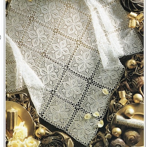 May include: A white crocheted tablecloth with a delicate floral pattern. The tablecloth is draped over a gold surface with decorative accents.