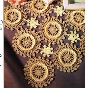 May include: A crocheted table runner with a brown and yellow color scheme. The runner features a repeating pattern of large, circular motifs with smaller, snowflake-shaped motifs in between.