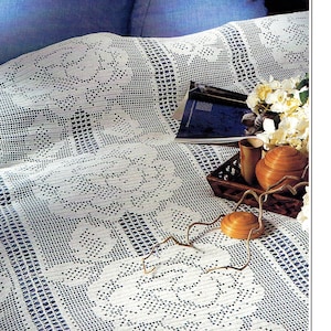 May include: A white crocheted throw blanket with a floral pattern. The blanket is draped over a blue sofa and has a book and decorative items on top of it.