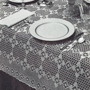 Könnte beinhalten: Eine weiße Häkeltischdecke mit einem zarten Blumenmuster. Die Tischdecke ist mit zwei Tellern, zwei Gläsern, Besteck und einer Schale Trauben gedeckt.