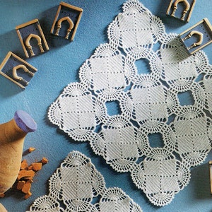 Könnte beinhalten: Drei weiße Häkeldeckchen mit einem zarten, filigranen Muster. Die Deckchen sind auf einem blauen Hintergrund mit kleinen Dekorationsgegenständen angeordnet.