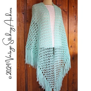 Może przedstawiać: Jasno błękitny szal wykonany na szydełku z frędzlami. Szal jest zarzucony na białą koszulę i drewniane tło.