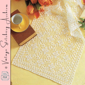 May include: A vintage-style, open-weave, white lace doily with a floral pattern. A yellow teacup and saucer sit on a brown book. The doily is on a yellow surface, with orange tulips in the background.