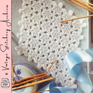 Pode incluir: Uma toalha de mesa branca de crochê com um padrão floral. A toalha de mesa é cercada por paus de canela, uma fita azul e um prato decorativo. A imagem também inclui o texto "Vintage Stitchery Archives" e um ícone PDF.