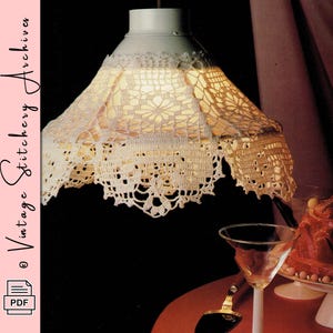 May include: A vintage-style lampshade with a white, crocheted design. The lampshade is suspended from the ceiling, casting a warm glow. The image also includes a martini glass and a cake on a pedestal, suggesting a retro aesthetic.