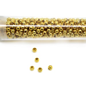 May include: A clear plastic tube filled with gold-colored round beads.  A few beads are scattered on a white surface.