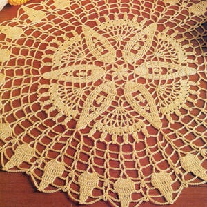 May include: A delicate, crocheted doily with a circular design featuring intricate floral motifs. The doily is made of a fine, cream-colored yarn and has a delicate, lacy texture.